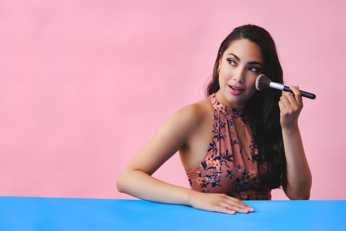 Surprised Hispanic woman with long brown hair holding large make up brush, copy space