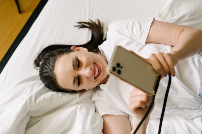 Happy woman using cellphone in bed at home