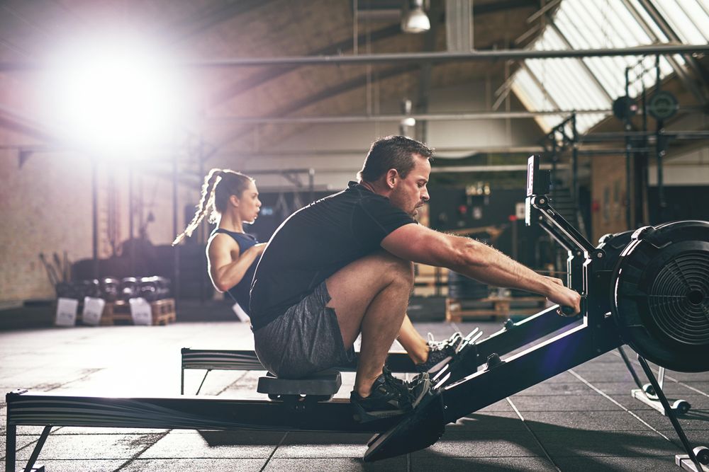 Healthy fit man using cardio machine beside woman at indoor gym facility