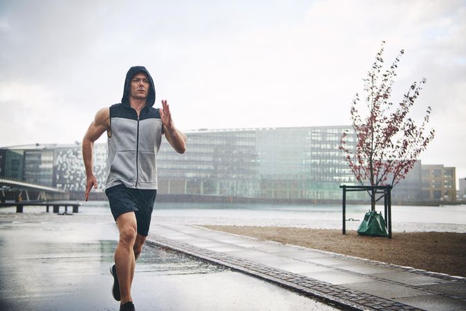 Muscular male in grey vest jogging outside on overcast day
