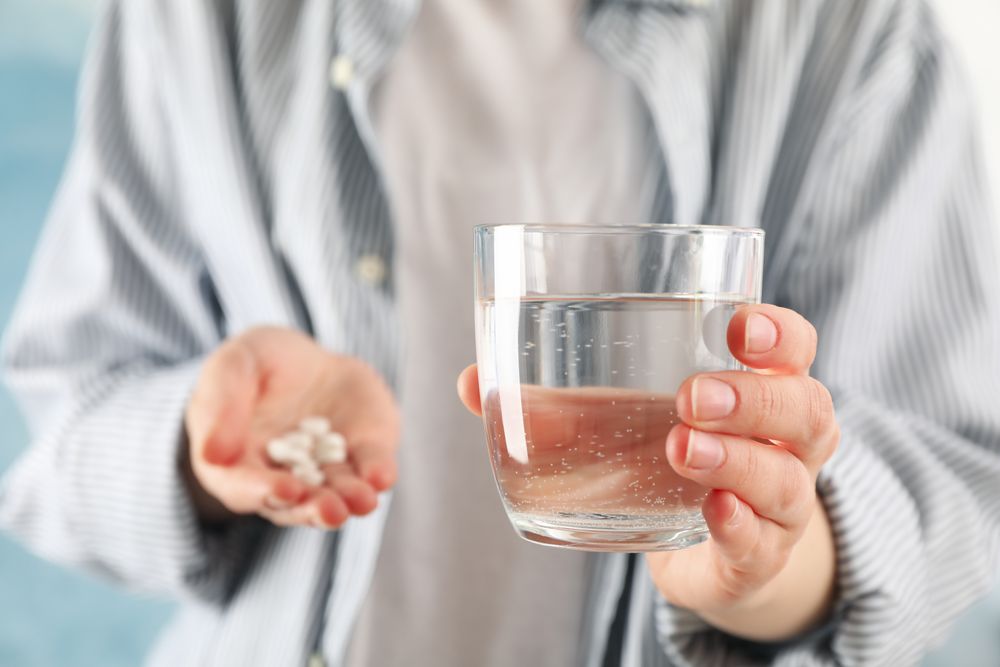 Torso of person holding medication in one hand and water in the other