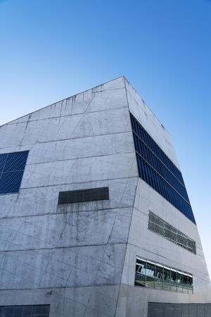 Grey modern building with unsymmetrical windows with blue sky, vertical
