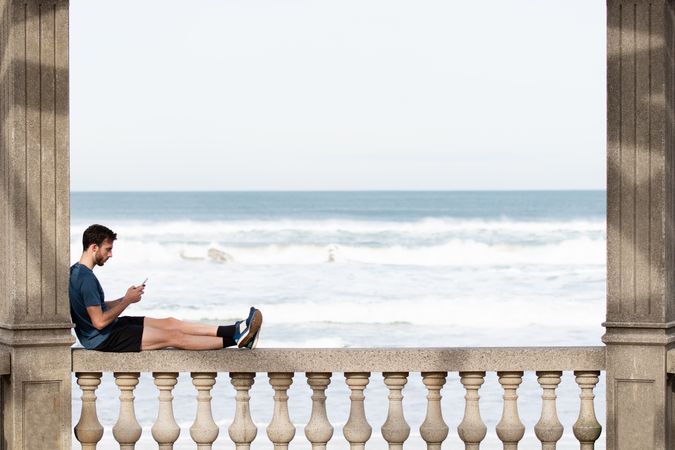 Man in sports clothing relaxing on fence using smartphone