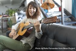 Female on sofa playing acoustic guitar while singing at home 0LgKXb