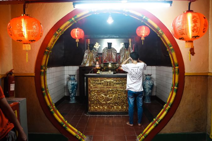 Back view of young man standing in front of shrine decorated with Chinese New Year lanterns
