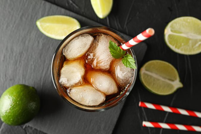 Glass with ice cola and tubule on background with limes