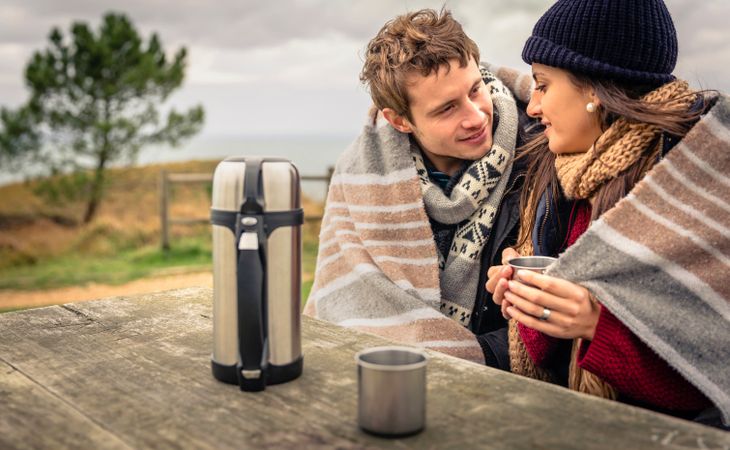 Couple kissing on park bench with flask of coffee on cold day