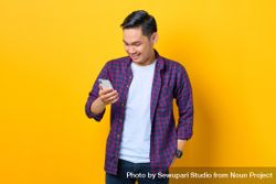 Smiling Asian man in plaid shirt  looking down at smartphone 56Kex4