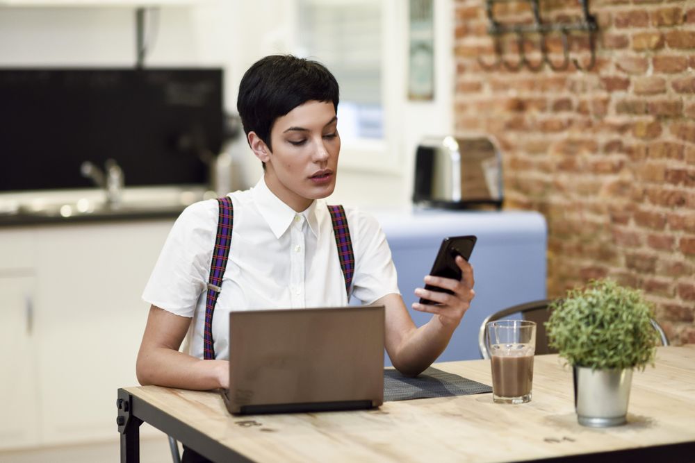 Woman in loft apartment reading her smart phone while working at home