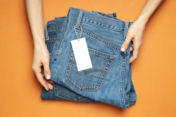 Folded jeans with a tag on an orange background