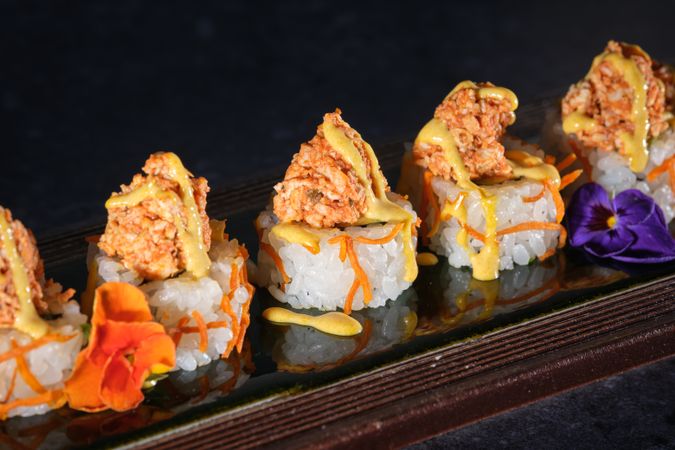 Appetizing sushi topped with salmon and fresh sauce served on wooden tray