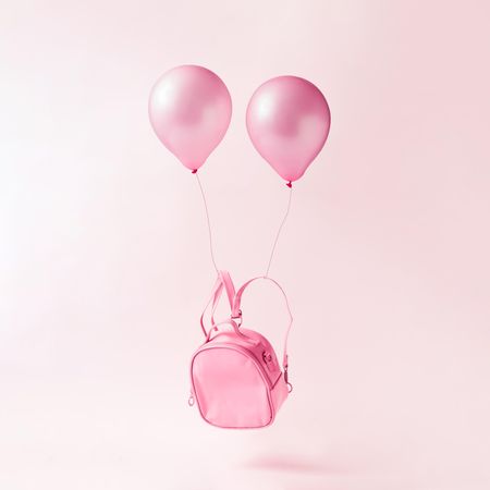 Pastel pink backpack bag with balloons floating on pink background