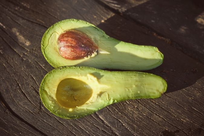 Halves of ripe avocado on wooden table