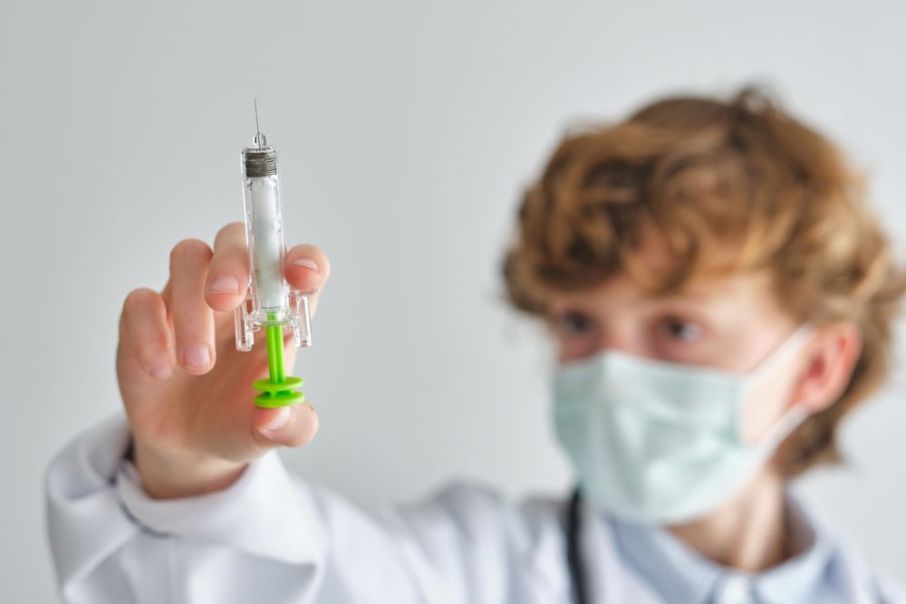 Attentive boy doctor in face mask with toy syringe
