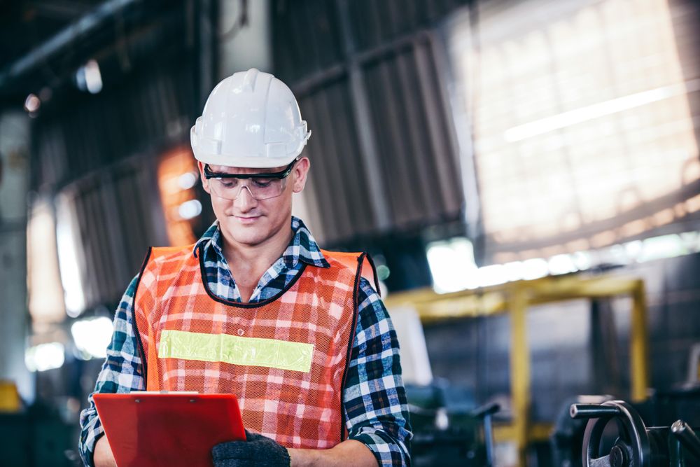 Front view of man in factory with PPE gear and clipboard