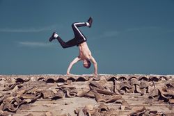 Flexible man performing tow handstand element of breakdance on rooftop
