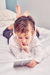 Boy lying on bed and watching video on tablet