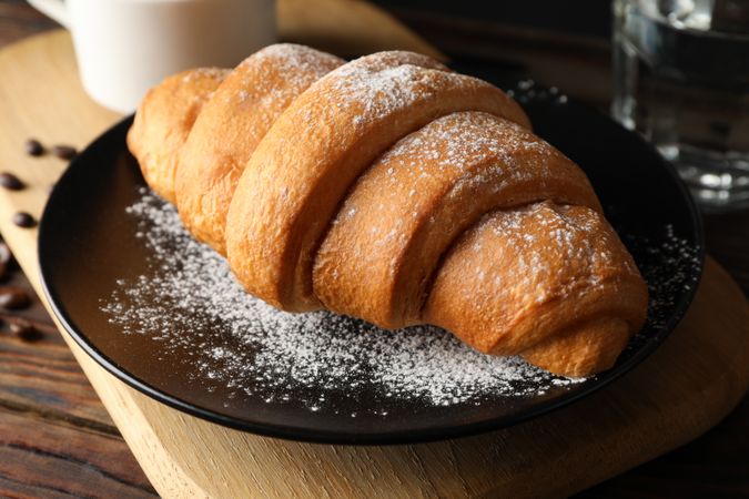 Delicious croissant on plate on wooden table with powdered sugar, close up