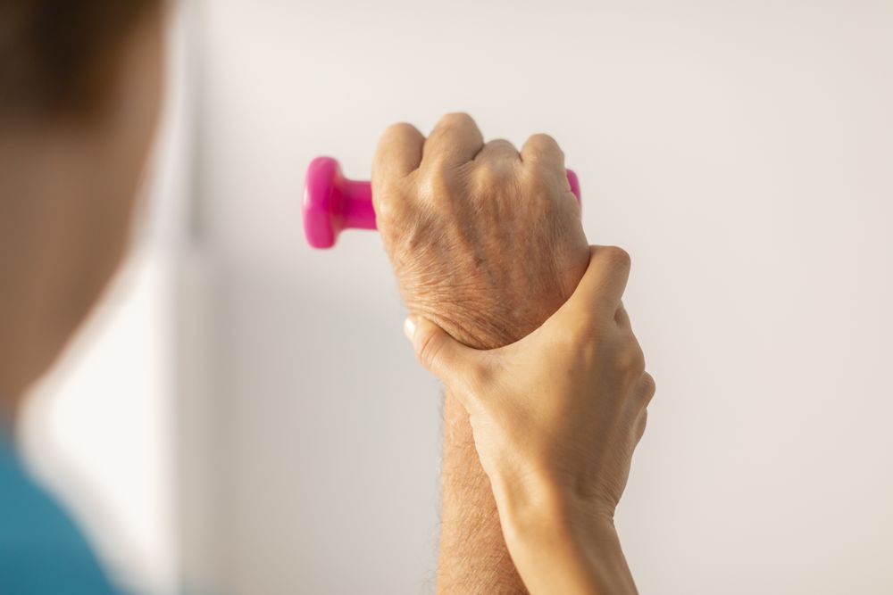A physical therapist performs a therapy session with a weight to rehabilitate the wrist and arm of an older man