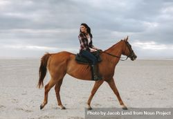 Woman horse rider on beach at sunset and glancing back 0KPyM5