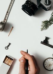 Hand holding pen above arrangement of vintage items on desk