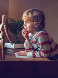 Cute schoolboy with book sitting at table
