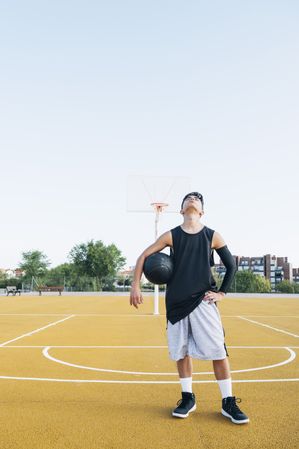 Young man playing on yellow basketball court outdoor.