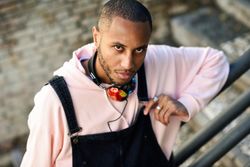 Serious male in overalls and hoodie leaning on railing of stairs outside