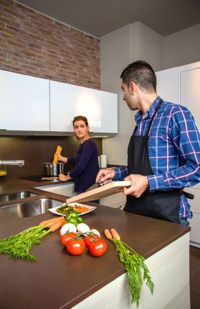 Couple in kitchen talking together preparing pasta for dinner