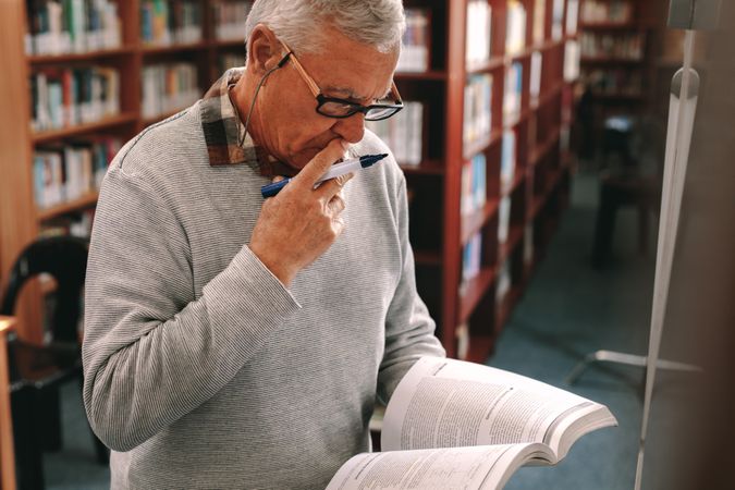 Mature man reading a book with concentration standing in classroom