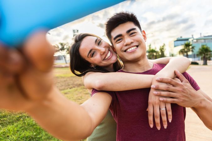 Pretty woman hugging Asian boyfriend while taking selfie portrait with mobile phone