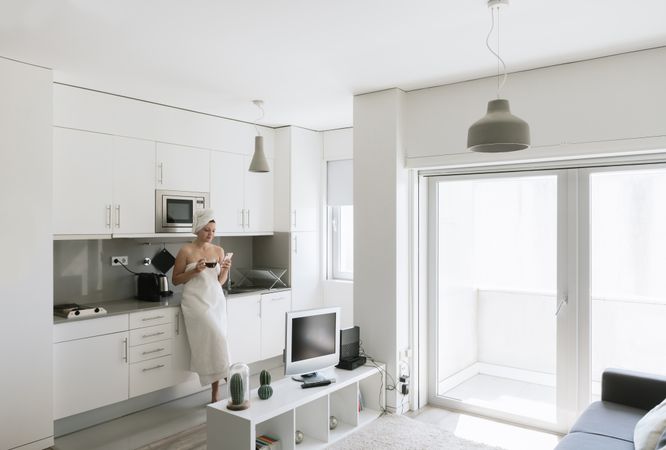 Joyful adult woman enjoying day off while having hot drink after bath in apartment with simple interior design