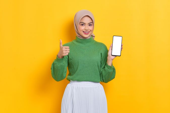 Woman in headscarf showing screen of her smart phone and giving the thumbs up