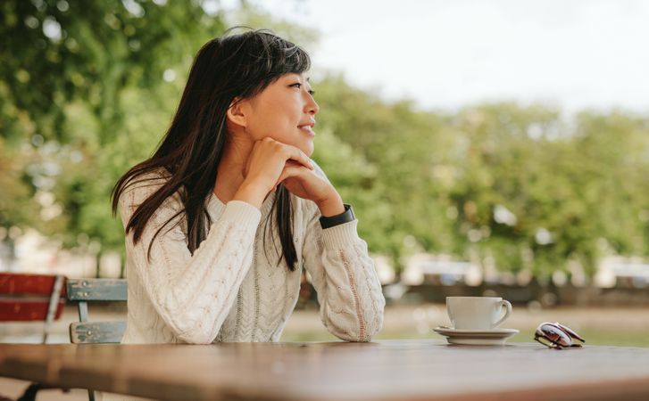 Happy young woman sitting at cafe with a cup of coffee on table and looking away