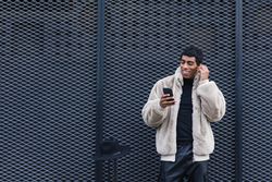 Content stylish hispanic man with smartphone in earbud on street