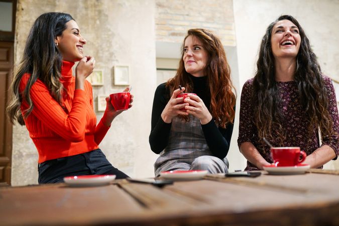 Three women laughing over drinks in coffee shop
