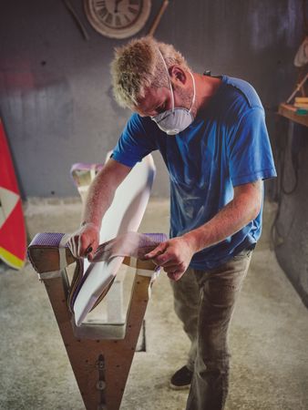 Attentive male surfboard shaper polishing template edges with sa
