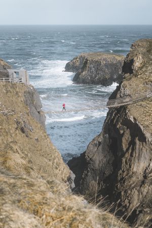 Tourist walking on rope bridge suspended between cliffs in Northern Ireland
