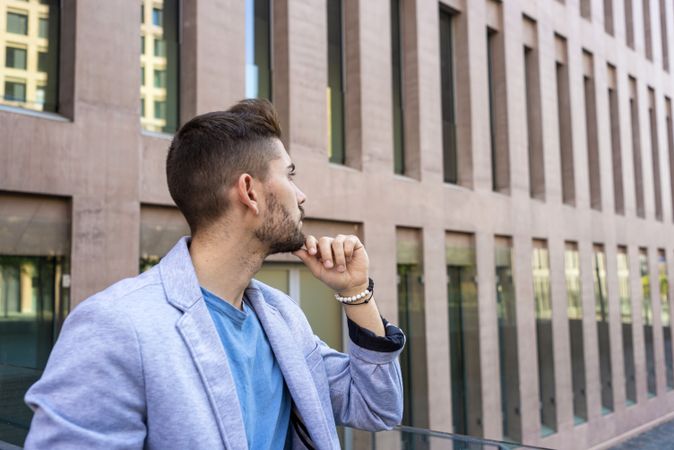 Pensive bearded young man outside building looking away with hand on chin