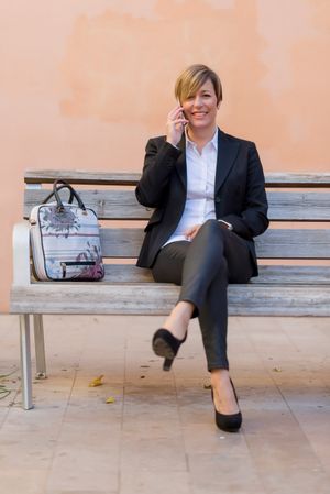 Content businesswoman sitting on bench speaking on phone
