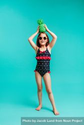 Stylish child in swimwear holding a green colored pineapple on her head 42RM74