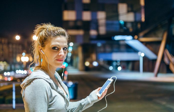 Portrait of young blonde woman looking at camera while listening music on mobile phone