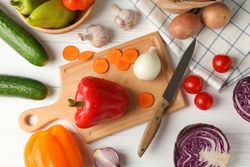 Vegetables, board and knife on wooden background, top view