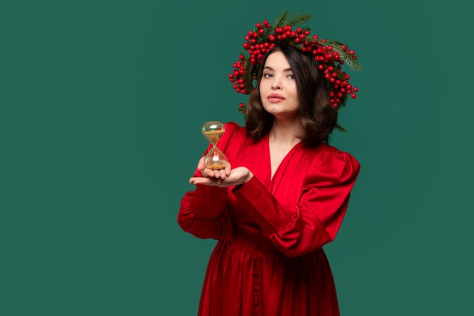 Woman with berry wreath holding hourglass thoughtfully.