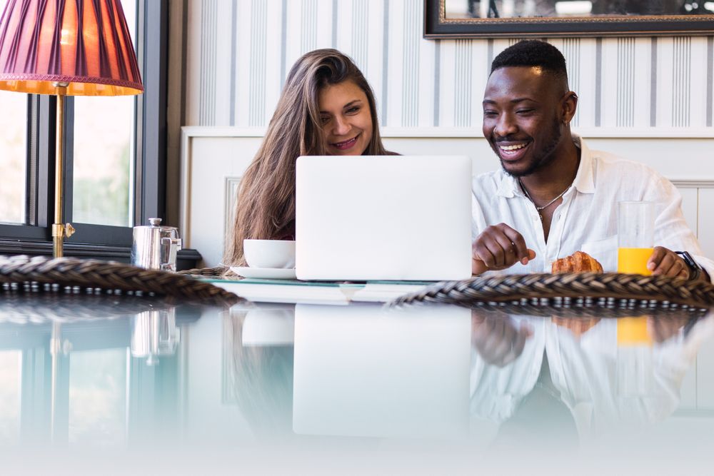 Cheerful multiethnic couple using laptop during breakfast at home