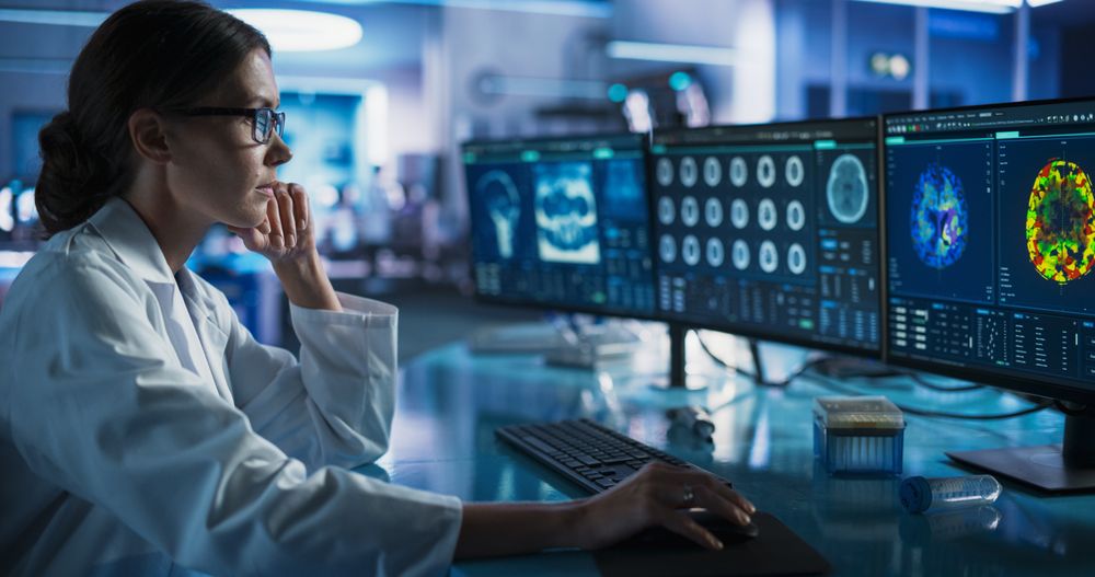 Medical Research Center Laboratory: Female Neurologist Using Desktop Computer With MRI And PET Scans Of a Brain.