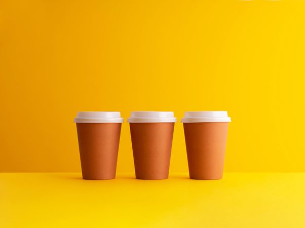 Three disposable coffee cups on yellow background