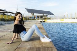 One happy young woman with long hair sitting on promenade while smiling and looking away