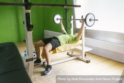 Man in green t-shirt lifting heavy bar exercising arms 5Q6DE4