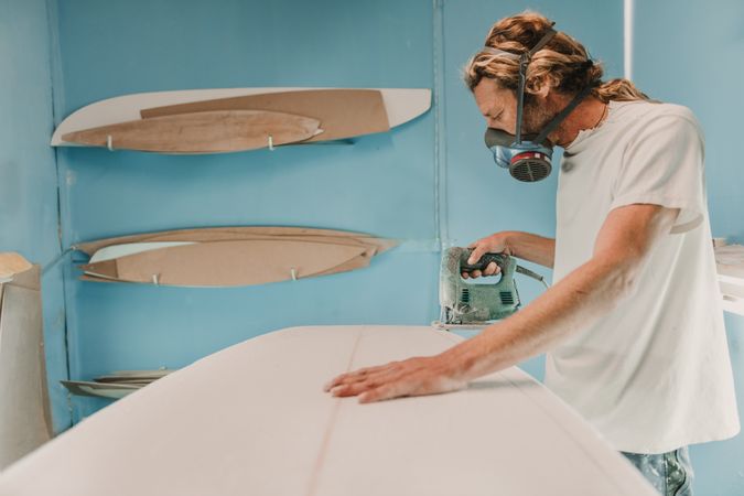Man with tool sawing surf board in workshop
